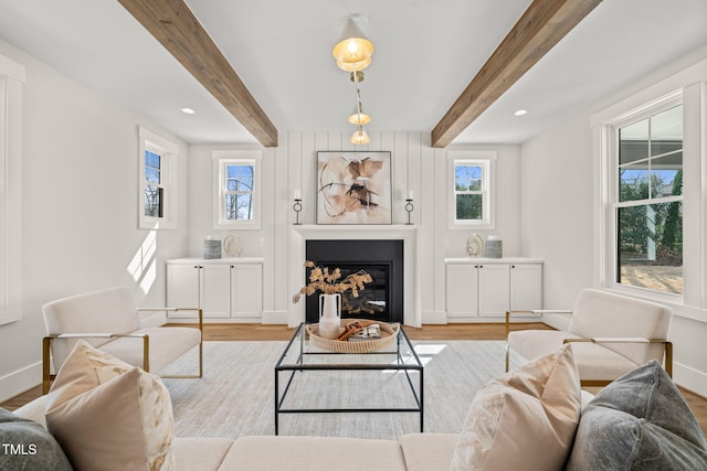 living area with baseboards, beam ceiling, recessed lighting, wood finished floors, and a glass covered fireplace