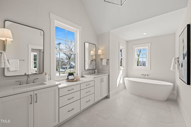 bathroom featuring double vanity, vaulted ceiling, a freestanding tub, and a sink