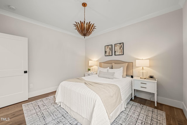 bedroom with ornamental molding, wood finished floors, baseboards, and a chandelier