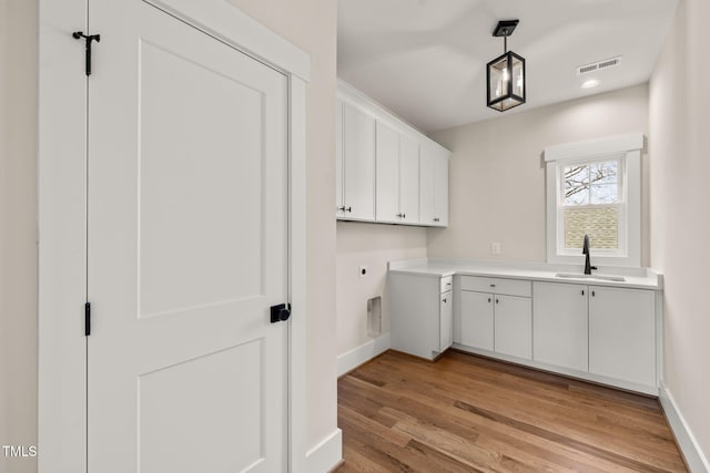 laundry area featuring visible vents, a sink, cabinet space, light wood finished floors, and baseboards