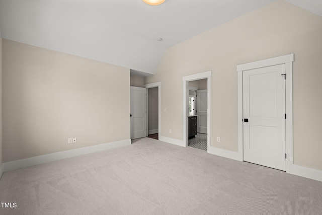 unfurnished bedroom with baseboards, ensuite bathroom, carpet flooring, and vaulted ceiling