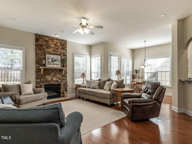 living area with ceiling fan with notable chandelier, dark wood-style flooring, a fireplace, and baseboards