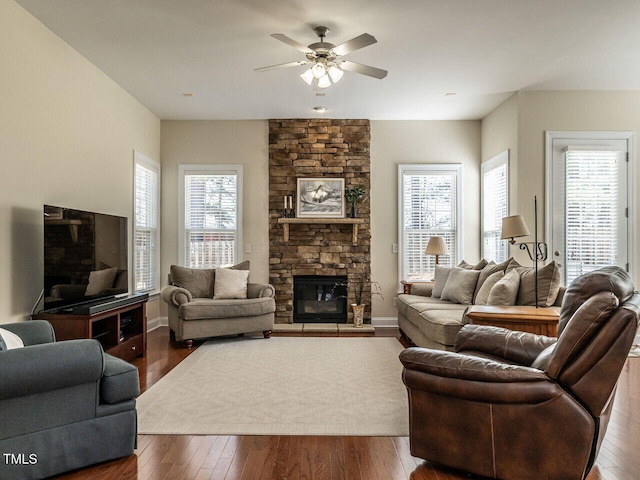 living room featuring ceiling fan, a fireplace, baseboards, and dark wood-type flooring