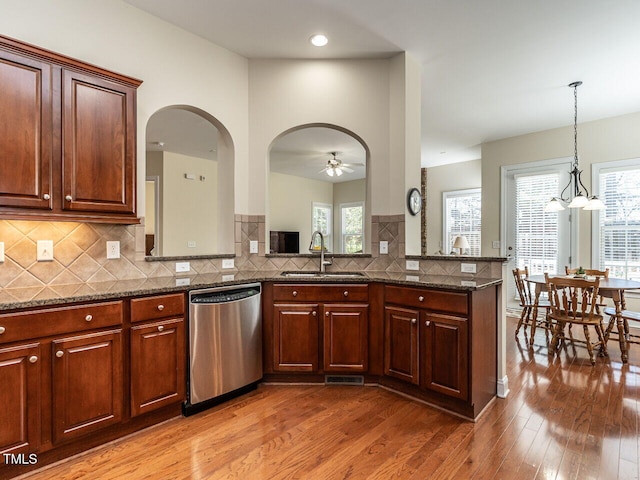 kitchen featuring a sink, stainless steel dishwasher, backsplash, light wood finished floors, and dark stone countertops