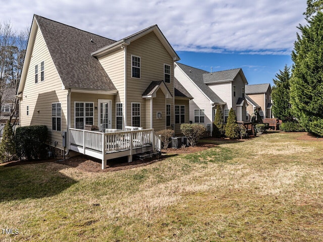 rear view of property featuring a shingled roof, a deck, and a lawn