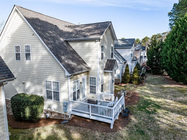 back of property with a shingled roof, a lawn, and a deck