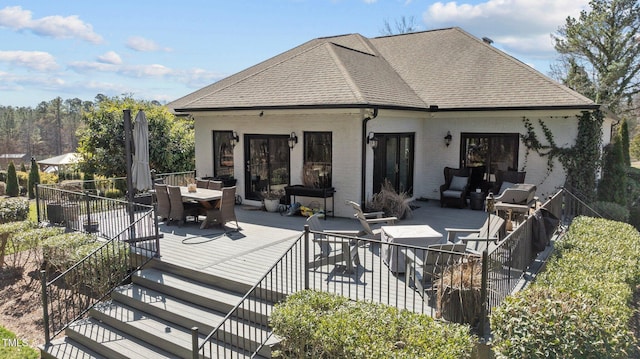 rear view of property with outdoor dining space, roof with shingles, a deck, outdoor lounge area, and brick siding