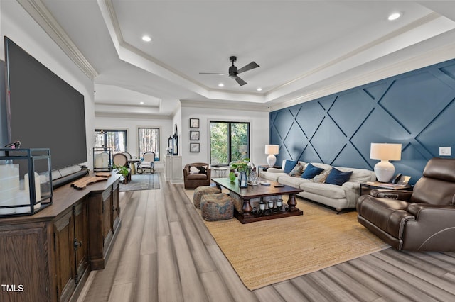 living room with light wood finished floors, a tray ceiling, crown molding, and recessed lighting