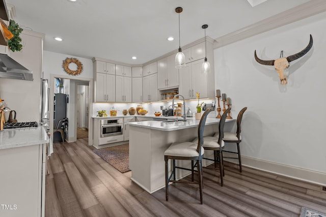 kitchen featuring decorative backsplash, light wood-style flooring, a breakfast bar area, stainless steel oven, and a sink