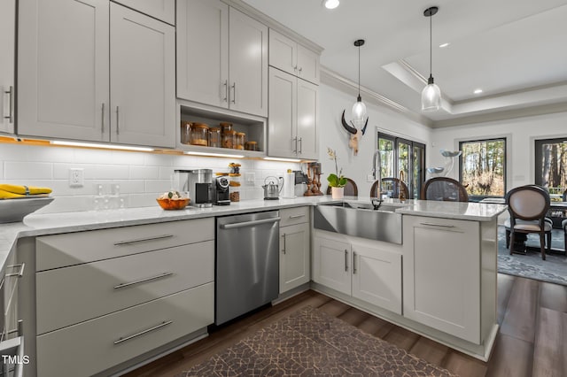 kitchen with a tray ceiling, dark wood-style flooring, tasteful backsplash, stainless steel dishwasher, and a peninsula