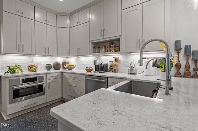 kitchen with tasteful backsplash, appliances with stainless steel finishes, a sink, and light stone countertops