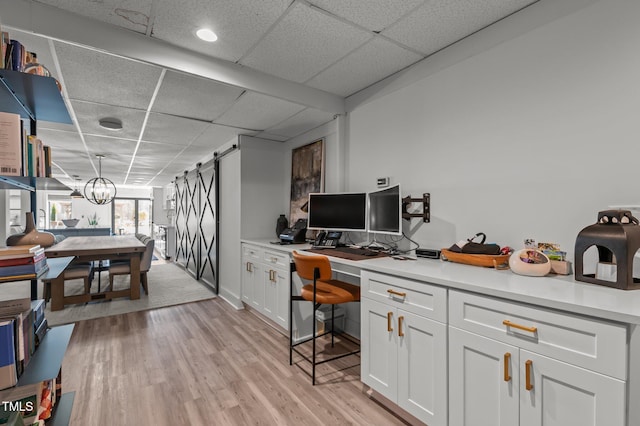 home office featuring a paneled ceiling, a barn door, light wood-style flooring, and a notable chandelier