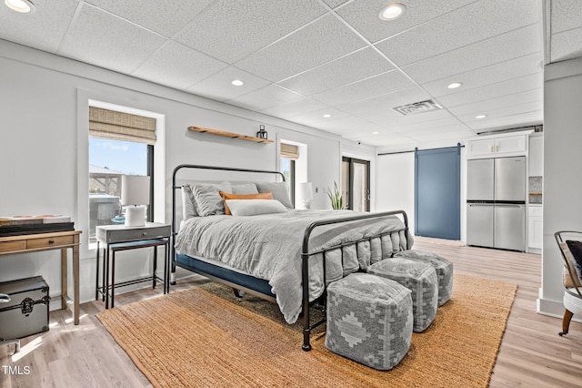 bedroom with a barn door, visible vents, stainless steel refrigerator, light wood-type flooring, and recessed lighting