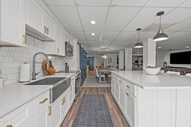 kitchen with stainless steel appliances, open floor plan, white cabinetry, a sink, and wood finished floors