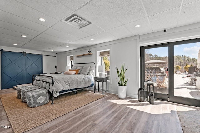 bedroom featuring wood finished floors, visible vents, a drop ceiling, and a barn door