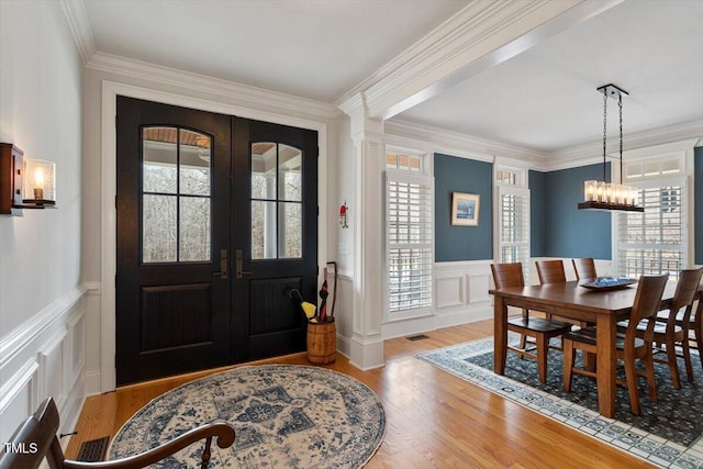 foyer featuring visible vents, wainscoting, ornamental molding, wood finished floors, and french doors