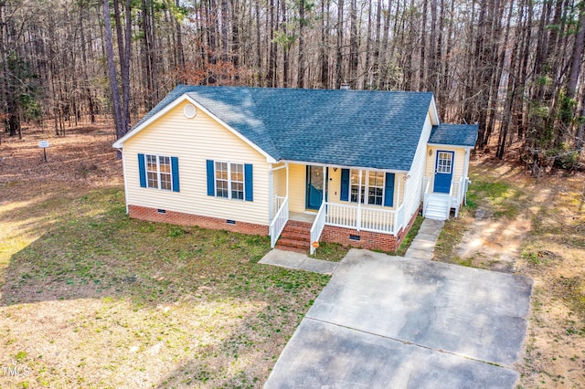 view of front of property with covered porch, a shingled roof, crawl space, a front yard, and a wooded view