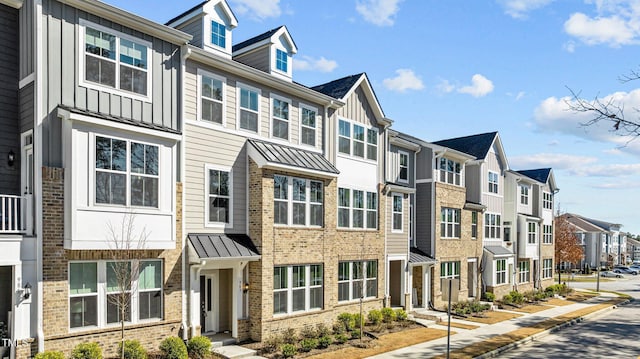 townhome / multi-family property with board and batten siding, a residential view, a standing seam roof, and brick siding