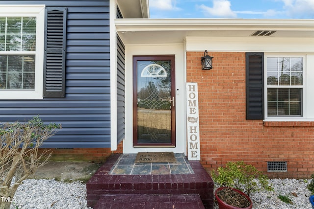 view of exterior entry with crawl space and brick siding