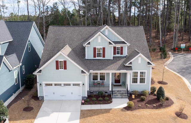 traditional home with covered porch, a garage, concrete driveway, roof with shingles, and board and batten siding