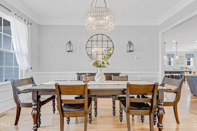 dining space featuring an inviting chandelier, light wood finished floors, crown molding, and a wainscoted wall