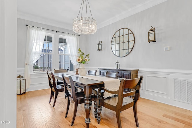 dining area featuring visible vents, wainscoting, light wood-style flooring, ornamental molding, and a chandelier