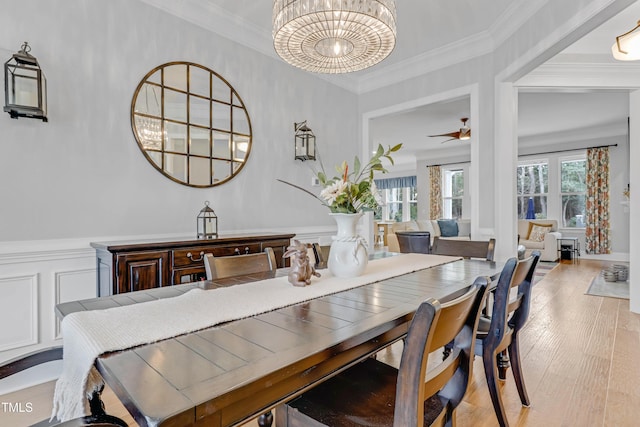 dining room with ceiling fan with notable chandelier, a wainscoted wall, wood finished floors, and crown molding