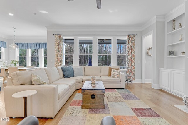 living area with light wood finished floors, built in shelves, baseboards, and crown molding