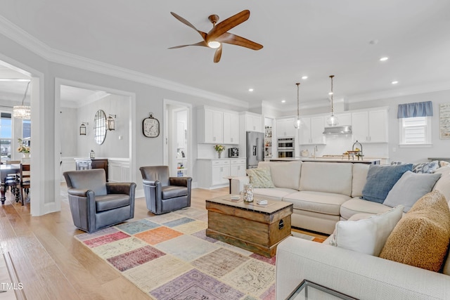 living room with recessed lighting, ceiling fan with notable chandelier, light wood-style floors, ornamental molding, and wainscoting