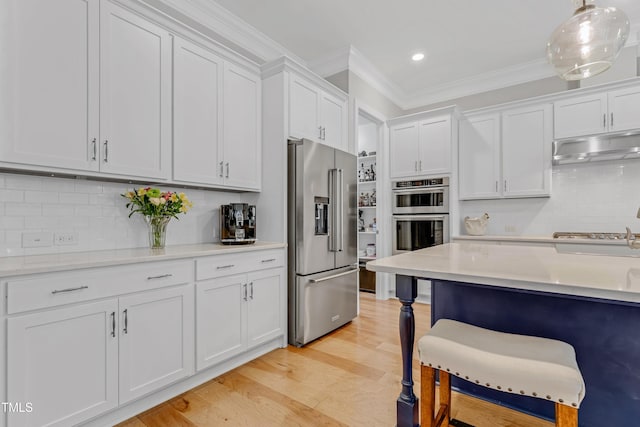 kitchen with under cabinet range hood, a breakfast bar, light countertops, ornamental molding, and appliances with stainless steel finishes