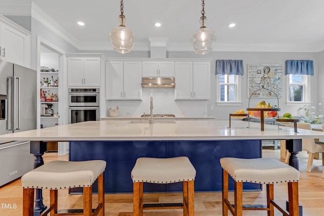 kitchen with under cabinet range hood, a breakfast bar, white cabinets, ornamental molding, and appliances with stainless steel finishes