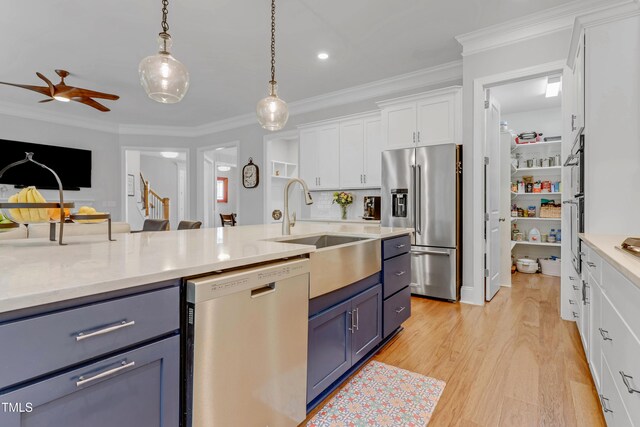 kitchen featuring blue cabinets, a sink, white cabinetry, appliances with stainless steel finishes, and crown molding