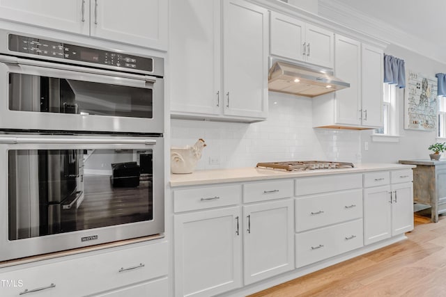 kitchen featuring white cabinets, stainless steel appliances, light countertops, under cabinet range hood, and backsplash