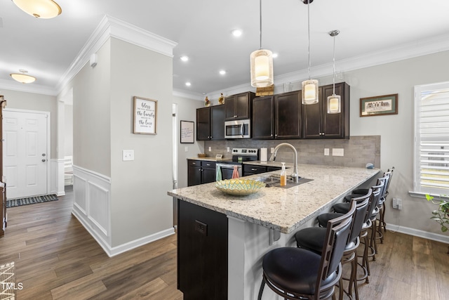 kitchen featuring dark wood-style floors, a breakfast bar area, tasteful backsplash, appliances with stainless steel finishes, and ornamental molding