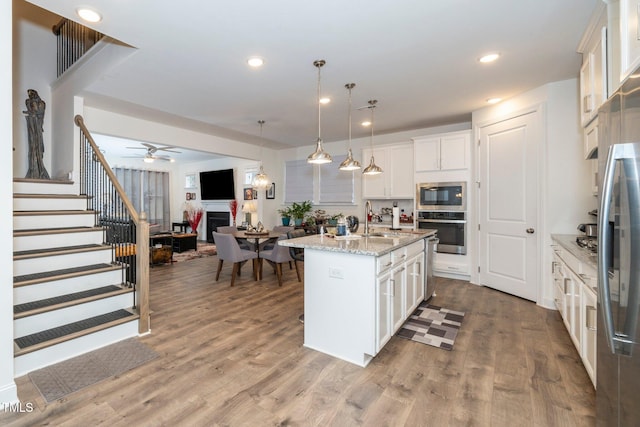 kitchen with light stone counters, pendant lighting, appliances with stainless steel finishes, white cabinets, and a kitchen island with sink