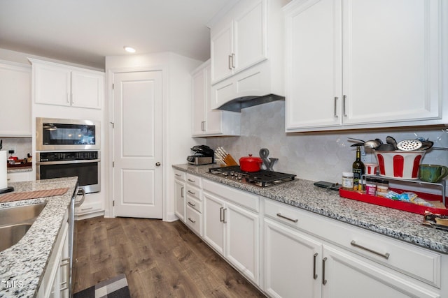 kitchen with appliances with stainless steel finishes, dark wood-style flooring, white cabinets, and tasteful backsplash