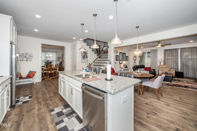 kitchen with an island with sink, hanging light fixtures, stainless steel appliances, white cabinetry, and a sink