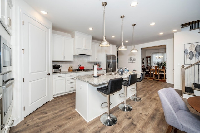 kitchen featuring decorative light fixtures, light stone countertops, a center island with sink, and white cabinets