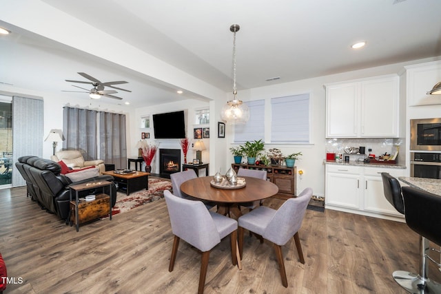 dining space with a ceiling fan, recessed lighting, a warm lit fireplace, and wood finished floors