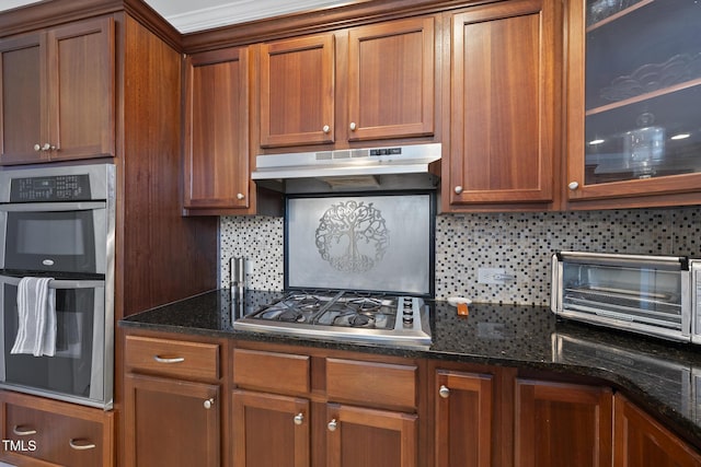 kitchen featuring glass insert cabinets, brown cabinetry, stainless steel appliances, and under cabinet range hood