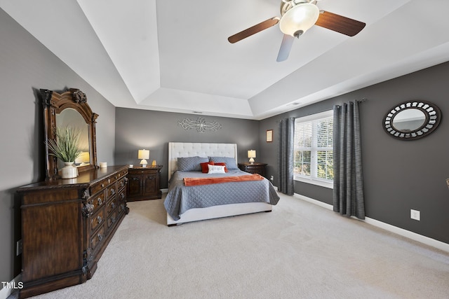 bedroom featuring light carpet, ceiling fan, a tray ceiling, and baseboards