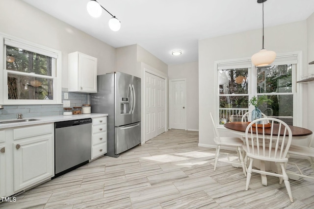 kitchen with white cabinets, a sink, stainless steel appliances, light countertops, and backsplash