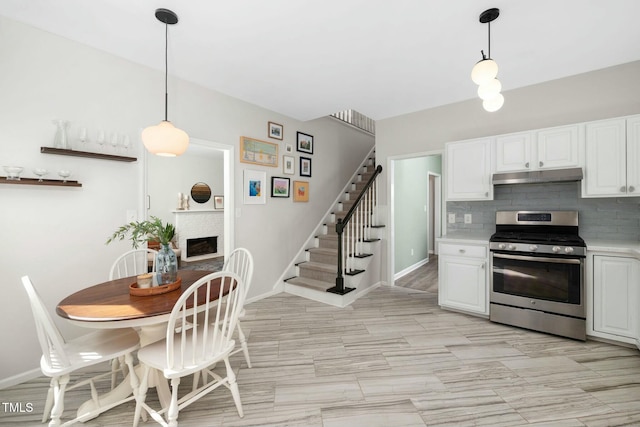 kitchen featuring stainless steel gas range oven, under cabinet range hood, a fireplace, white cabinets, and decorative backsplash