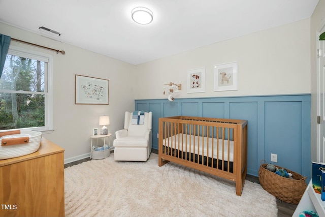 bedroom featuring a nursery area, visible vents, and a decorative wall