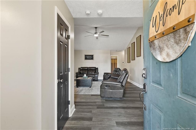 foyer entrance featuring baseboards, a ceiling fan, dark wood-style flooring, vaulted ceiling, and a textured ceiling