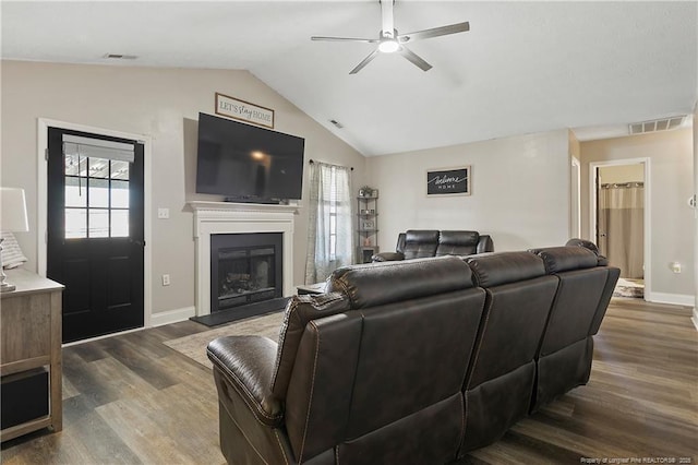 living room with a fireplace with raised hearth, visible vents, vaulted ceiling, and dark wood-style flooring