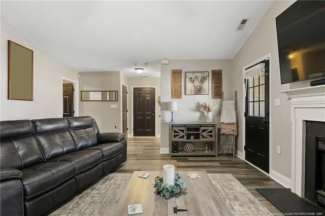 living room featuring dark wood-style flooring, visible vents, a fireplace, and baseboards