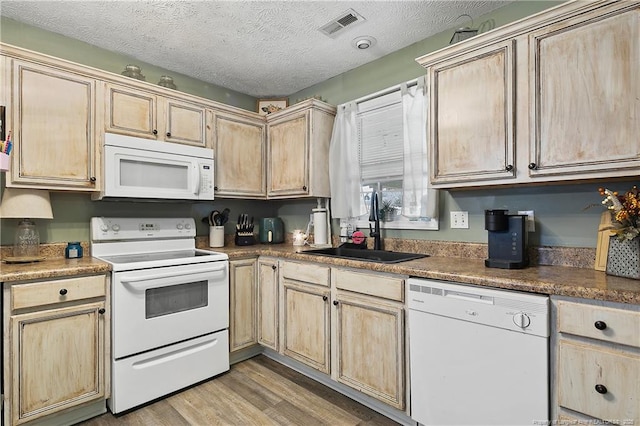 kitchen featuring visible vents, light wood-style flooring, light brown cabinets, a sink, and white appliances