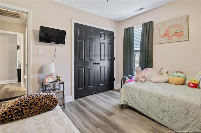 bedroom with a closet, light wood-type flooring, visible vents, and baseboards