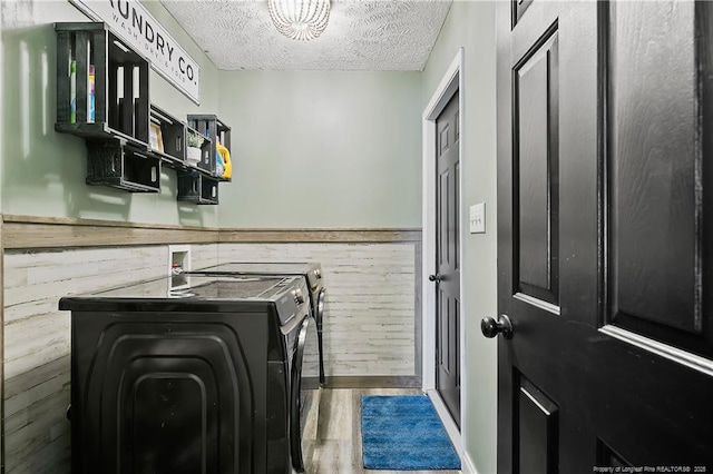 laundry area with a textured ceiling, washing machine and dryer, a wainscoted wall, laundry area, and wood finished floors